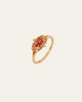 The Vivien Garnet Ring by CAMELLIA features an oval red gemstone, encircled by small clear stones on a delicate, hypoallergenic band.